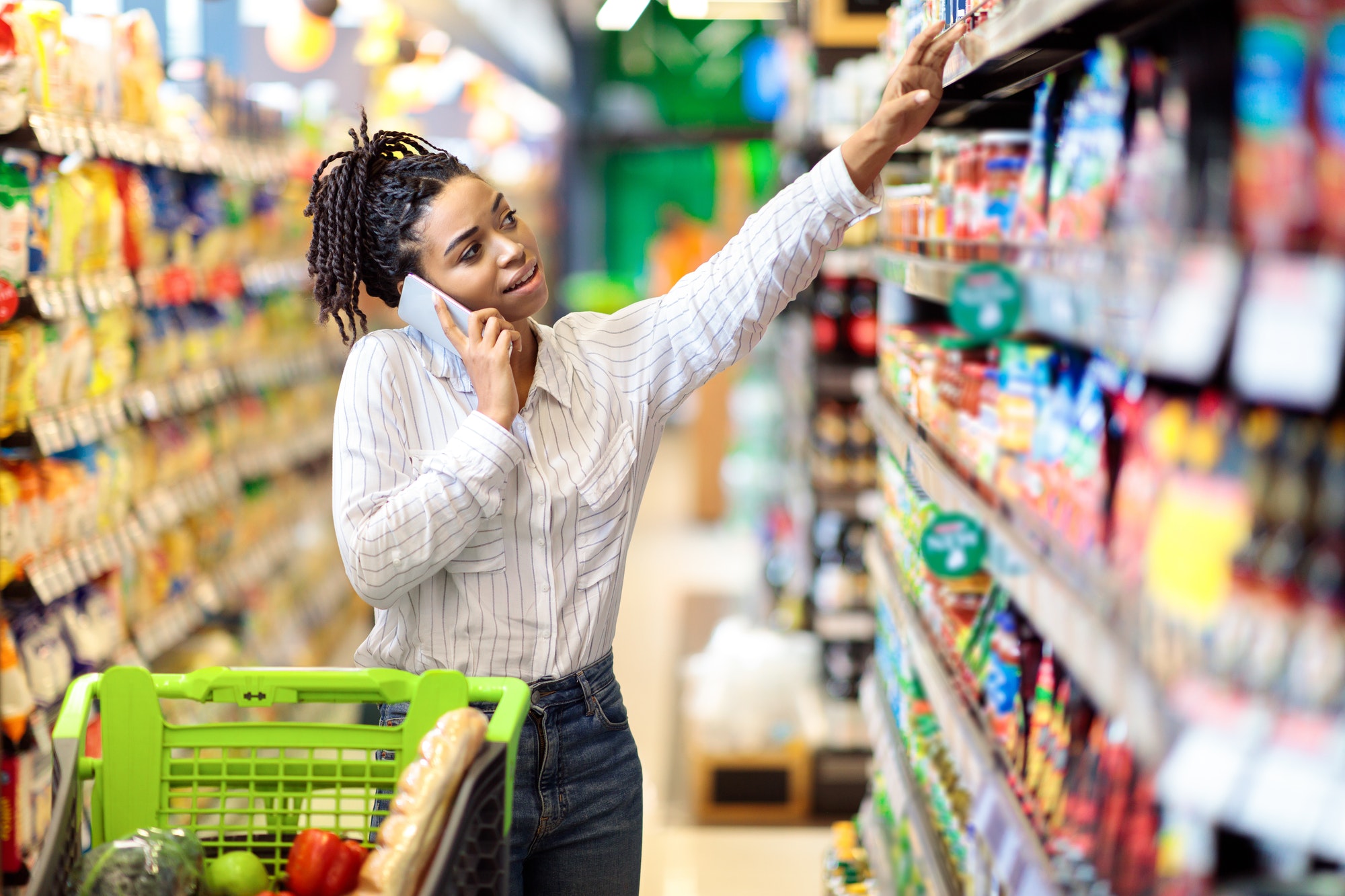 African Woman Talking On Mobile Phone Buying Food In Supermarket